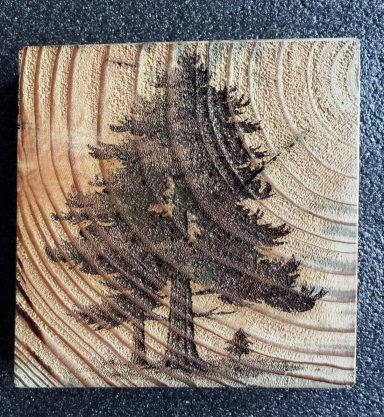 Wooden fence post slice with a silhouette of a tree on a textured surface.